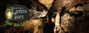 Woman walking with her back to the camera, on a dark trail in Ruby Falls cavern with a lantern lighting the path ahead of her.