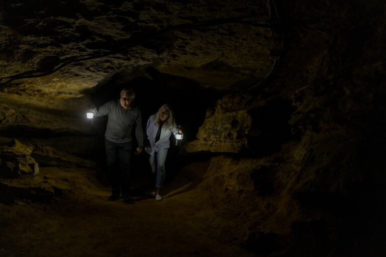 Man and woman explore the dark cave with handheld lanterns lighting the cavern trail